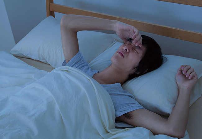 眠れずに額に手を載せる男性