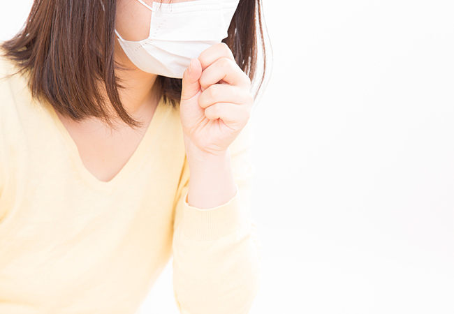 咳き込み口元に手を当てるマスクをした女性